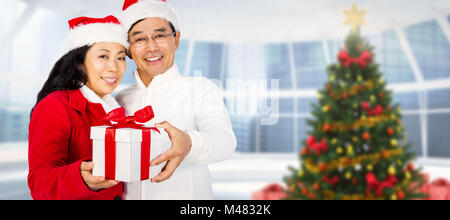 Composite image of festive senior couple exchanging gifts Stock Photo