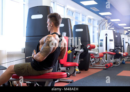 At gym. Tattooed bodybuilder trains on simulator Stock Photo