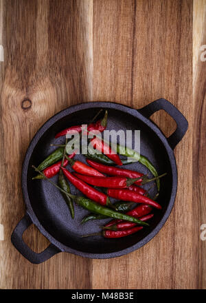 Red and Green Chillies in a black cast Iron bowl on a vertical wooden background with copy space Stock Photo