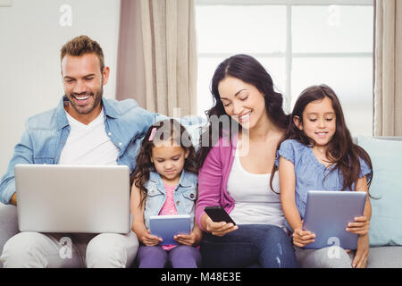 Family using modern technologies while sitting on sofa Stock Photo