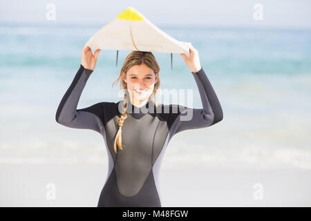 Portrait of woman in wetsuit carrying surfboard over head Stock Photo