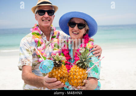 Happy senior couple wearing a garland and holding pineapple cocktail Stock Photo