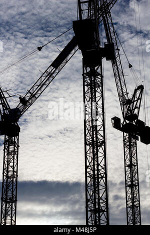Three tower cranes silhouetted against a cloud filled sky Stock Photo
