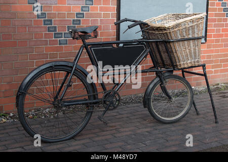 An old vintage delivery bike standing and complete with a wicker basket on the front Stock Photo