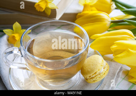Cup of hot tea, yellow tulips and lemon macaroons Stock Photo