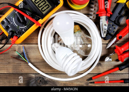 Light bulbs inside a white roll of electric cable and work tools on an antique wooden desk. Stock Photo