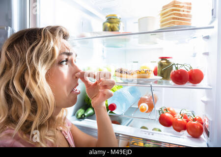Close-up Of A Young Woman Holding Her Nose Near Foul Food In Refrigerator Stock Photo