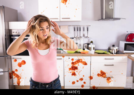 Portrait Of A Worried Young Woman Standing In Dirty Kitchen At Home Stock Photo