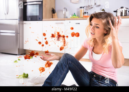 Portrait Of A Worried Young Woman Sitting In Dirty Kitchen At Home Stock Photo