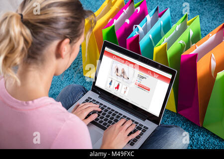 Close-up Of Woman Shopping Online Using Laptop With Colorful Shopping Bags On Carpet Stock Photo