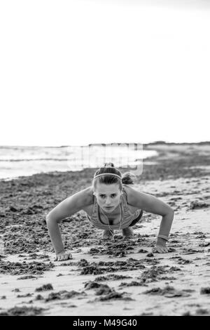 Refreshing wild sea side workout. active sportswoman in sports gear on the seashore doing pushups Stock Photo