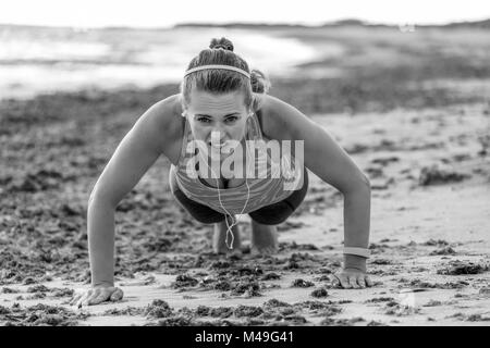 Refreshing wild sea side workout. young fit woman in sports gear on the seashore doing pushups Stock Photo