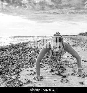 Refreshing wild sea side workout. healthy woman in sport clothes on the beach doing pushups Stock Photo