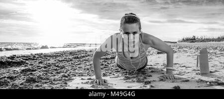Refreshing wild sea side workout. young sportswoman in sport clothes on the seashore doing pushups Stock Photo