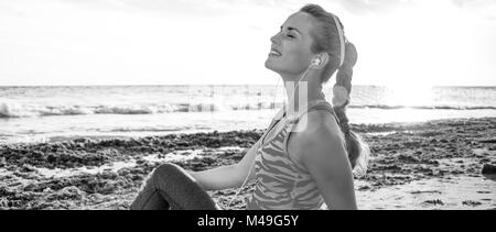 Refreshing wild sea side workout. relaxed healthy active woman in sportswear sitting on the seashore Stock Photo