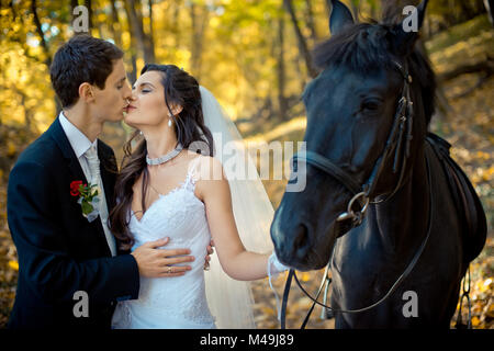 Stylish newlywed couple kissing during their walk with horse along the autumn forest. Romantic wedding portrait. Stock Photo