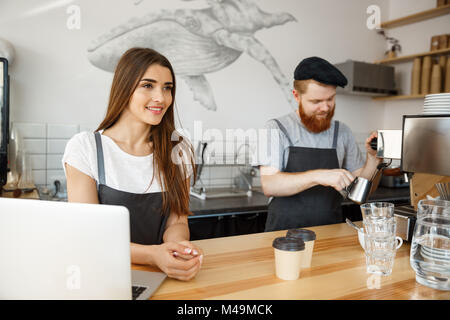 Coffee Business Concept - Positive young bearded man and beautiful attractive lady barista couple enjoy working together at the modern coffee shop Stock Photo