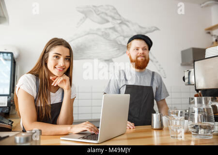 Coffee Business Concept - Cheerful baristas looking at their laptop for online orders in modern coffee shop. Stock Photo