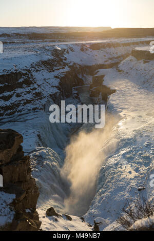 Spray rising from partially frozen, icy lower Gullfoss waterfall (part of the 'Golden Circle') in Iceland on a sunny winter day Stock Photo