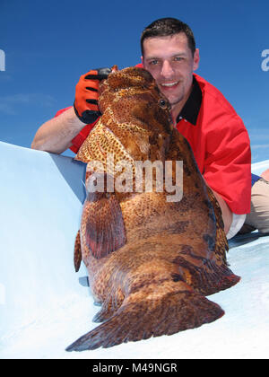 Happy  fisherman holding a beautiful grouper fish. Deep sea fishing, big game fishing, catch of fish. Stock Photo