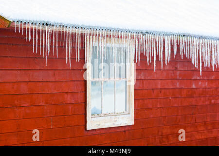 Icicles hanging from the roof of a red wooden building. Stock Photo