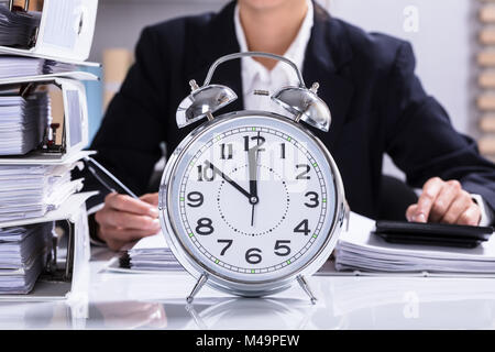 Businessperson Working In Office With Clock And Stacked Folders On Desk Stock Photo
