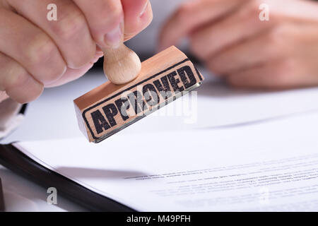 Close-up Of Person Hands Using Stamper On Document With The Text Approved Stock Photo