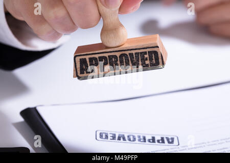 Close-up Of Person Hands Using Stamper On Document With The Text Approved Stock Photo