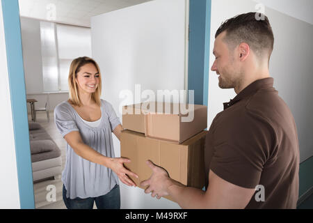 Happy Young Woman Accepting Parcel Box From Delivery Man Stock Photo