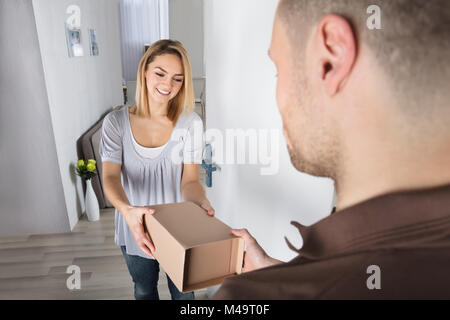 Happy Young Woman Accepting Parcel Box From Delivery Man Stock Photo