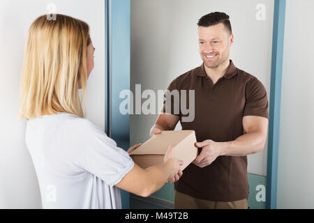 Happy Young Woman Accepting Parcel Box From Delivery Man Stock Photo