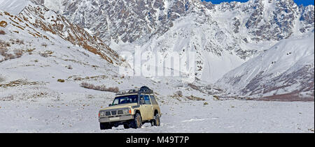 the car going on the snow plain against the background of snow-covered mountains and a glacier Stock Photo