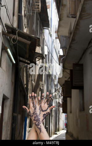 Woman's henna decorated hands clasped upright in an alleyway in Stone Town, Zanzibar, Tanzania on a bright and sunny day
