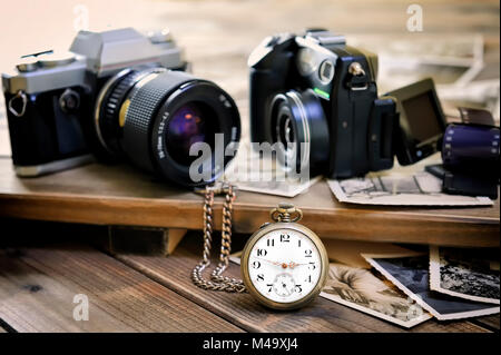 Close up antique pocket watch, vintage photographic prints, film camera and digital compact on aged wooden background. Stock Photo