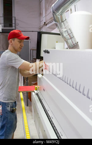 View at handsome young man working in the furniture factory. industrial carpenter worker operating wood cutting machine during wooden door furniture m Stock Photo