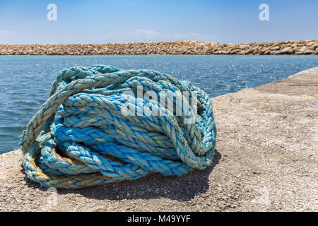 Coiled blue mooring rope at water in greek cave Stock Photo