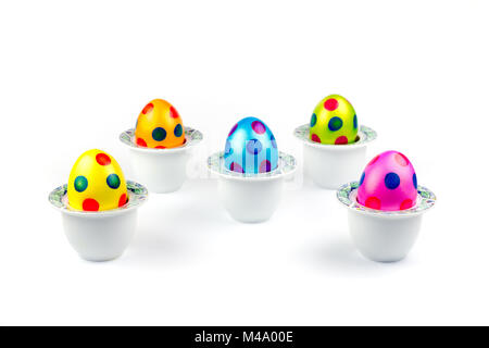 Painted easter eggs standing in porcelain egg cups on white