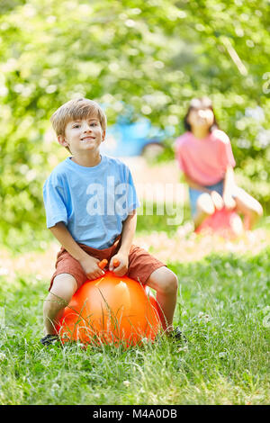 Boy is jumping on a ball at the kid's birthday in the park in summer Stock Photo