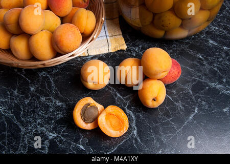 Ripe organic apricots harvested at summer time and big glass jar with canned sweet apricot compote on dark marble. Composition in rustic style - organ Stock Photo