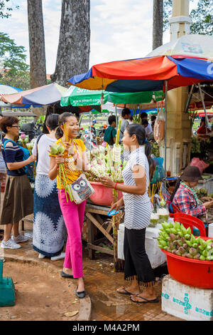 Happy local young women buying and selling votive offerings at a market stall at Ya Tep Shrine, Independence Gardens, Siem Reap, Cambodia Stock Photo