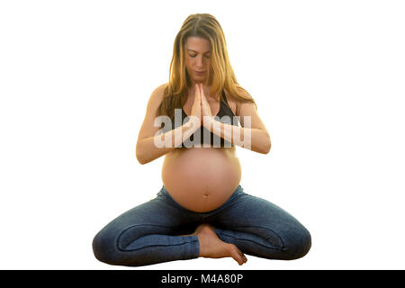 Yogini pregnant woman is practising yoga while sitting down against isolated white background. Stock Photo
