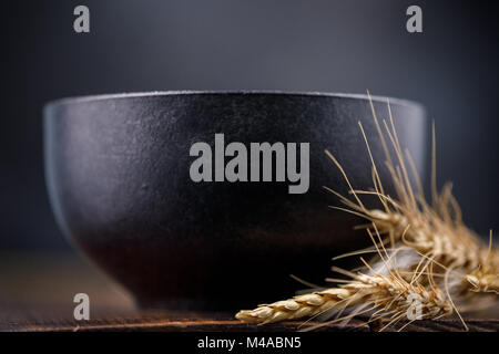 Refined black ceramic bowl and dried ears on a wooden background. Stock Photo