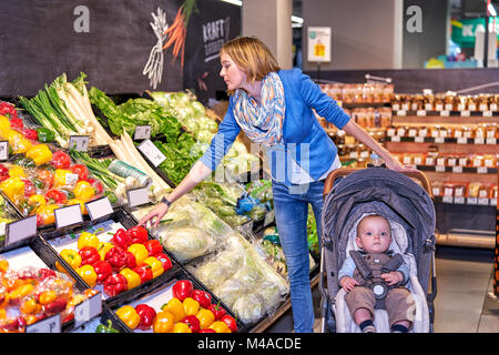 Woman in blue jacket and jeans choosing vegetables Stock Photo