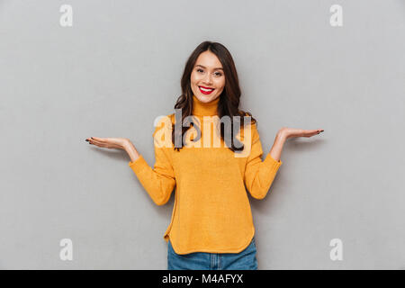 Happy brunette woman in sweater choosing something and looking at the camera over gray background Stock Photo