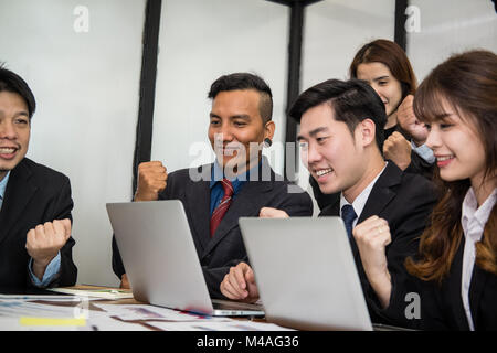 business team raise hands with happiness for successful project. cheerful asian businessman & businesswoman showing gladness for achievement Stock Photo