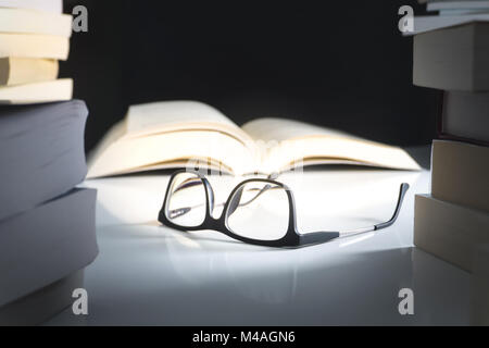 Glasses and open book on table surrounded by literature. Education, learning and reading concept. Stock Photo