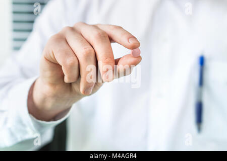 Doctor or pharmacist holding one pill between fingers. Medical professional and expert in white coat with medicine. Stock Photo