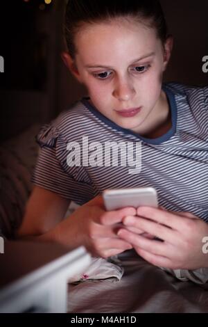 Young Girl Victim Of Bullying By Text Message Lying On Bed At Night Stock Photo