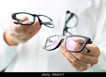 Optician comparing lenses or showing customer different options in spectacles. Eye doctor showing new glasses. Professional optometrist in white coat.