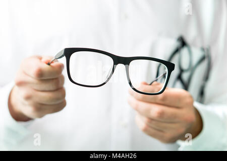 Optician holding glasses. Eye doctor showing new lenses. Professional optometrist in white coat.